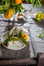 Table setting with white plate, cutlery, linen napkin and orange tree branch decoration on gray linen tablecloth . Close