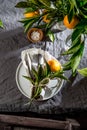 Table setting with white plate, cutlery, linen napkin and orange tree branch decoration on gray linen tablecloth . Close