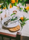 Table setting with white plate, cutlery, linen napkin and orange tree branch decoration on white linen tablecloth