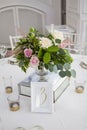 Table setting with a white tablecloth, beautiful flowers in vases, candlesticks. A tablet on the table for guests is three Royalty Free Stock Photo