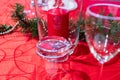 Table setup lunch in red for celebration. Shiny glass cup, red tablecloth, candles and decorations with green Christmas tree. Royalty Free Stock Photo