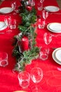 Table setup lunch in red for celebration. Shiny glass cup, red tablecloth, candles and decorations with green Christmas tree. Royalty Free Stock Photo