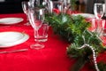 Table setup lunch in red for celebration. Shiny glass cup, red tablecloth, candles and decorations with green Christmas tree. Royalty Free Stock Photo