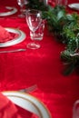 Table setup lunch in red for celebration. Shiny glass cup, red tablecloth, candles and decorations with green Christmas tree. Royalty Free Stock Photo