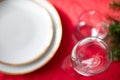 Table setup lunch in red for celebration. Shiny glass cup, red tablecloth, candles and decorations with green Christmas tree. Royalty Free Stock Photo