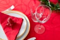 Table setup lunch in red for celebration. Shiny glass cup, red tablecloth, candles and decorations with green Christmas tree. Royalty Free Stock Photo