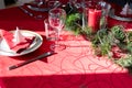 Table setup lunch in red for celebration. Shiny glass cup, red tablecloth, candles and decorations with green Christmas tree. Royalty Free Stock Photo