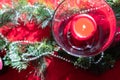 Table setup lunch in red for celebration. Shiny glass cup, red tablecloth, candles and decorations with green Christmas tree. Royalty Free Stock Photo