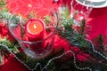 Table setup lunch in red for celebration. Shiny glass cup, red tablecloth, candles and decorations with green Christmas tree. Royalty Free Stock Photo
