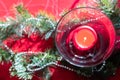 Table setup lunch in red for celebration. Shiny glass cup, red tablecloth, candles and decorations with green Christmas tree. Royalty Free Stock Photo