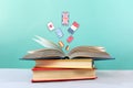 On the table is a stack of books, with an open book on top, from which flags fly out. Turquoise background. The concept Royalty Free Stock Photo