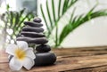 Table with stack of stones, flower and green leaves on background, space for text. Zen concept