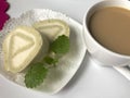 On the table stand a plate with a ready sliced roll, decorated with lemon bald leaves. A cup of coffee.