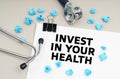 On the table is a stethoscope, blue crumpled pieces of paper and a sign with the inscription - INVEST IN YOUR HEALTH Royalty Free Stock Photo