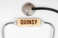 On the table is a stethoscope and a wooden plate with the inscription - quinsy