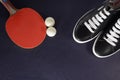 Table tennis racket, balls and black sneakers with white laces on a dark background Royalty Free Stock Photo