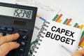 On the table there is a calculator, reports with graphs and a notepad with the inscription - CAPEX BUDGET