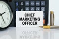On the table there is a clock, a pen, a calculator and a business card on which the text is written - CHIEF MARKETING OFFICER