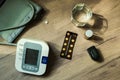 On the table there are pills, a blood pressure measuring device, a glass of water and an oxyometer. An elderly person`s kit. Top