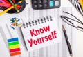 On the table there are reports, a calculator, colored pencils and stickers, a pen and a notebook with the text KNOW YOURSELF Royalty Free Stock Photo