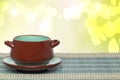 Table top on bowl background. Empty brown ceramic soup bowl on plate on a green bamboo straw mat over abstract bright yellow