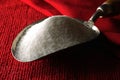 WHITE GRANULES OF SUGAR IN A METAL VINTAGE SCOOP ON A RED DISHCLOTH