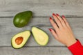 Table top view - avocado cut in half, woman hand with red nails