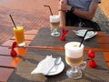 Table with two glasses of cappuccino, orange juice, three candies in red wrapper