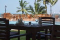 A table for two people near a swimming pool with green palm trees