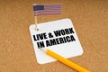 On the table is the US flag and a sheet of paper from a notebook with the inscription - Live and Work In America