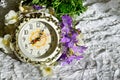 On the table is a vintage alarm clock and a bouquet of flowers.