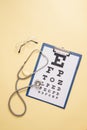 Table for visual acuity test and medical stethoscope is in yellow background. Concept of eye diagnosis, detection of eye diseases