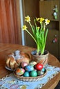 A table with a weave basket with multicolored dyed eggs, a pot with spring flowers and a sweet Easter bread