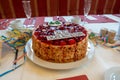 Table with a white tablecloth there is a red birthday strawberry cake with the inscription
