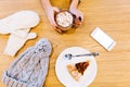 Table with white winter gloves, phone, hot chocolate holding by girl and piece of pie, knitted grey hat. Royalty Free Stock Photo