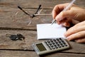 a table and a woman& x27;s hand writes with a pen on a sheet of paper next to it lies a calculator, keys and glasses, a Royalty Free Stock Photo