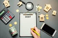 Table with wooden houses, calculator, coins, magnifying glass with the word Debt. The concept of debt for housing. Mortgage.