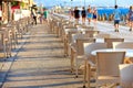 The tables and chairs of the beach cafe are located along the promenade among people walking near the blue sea in blur Royalty Free Stock Photo