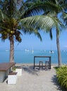 Tables and chairs on the beach with palm tree and yachts. Ocean landscape with boats as background.