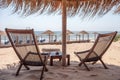 Tables and chairs set up in the beach. Wooden post with tropical umbrella standing above. Ocean breeze swaying the dry leaves. Res