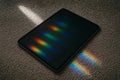 Tablet with black screen on textured beige carpet showing vibrant rainbow reflection matching carpet pattern beside it Royalty Free Stock Photo