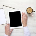 Tablet with blank screen in female hands. Feminine workspace with notepad and latte ice, overhead view. Top view. From above