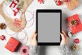 Tablet with a blank screen in a woman& x27;s hands surrounded by Christmas decorations and gifts, mockup for advertising Royalty Free Stock Photo