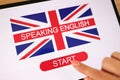 Tablet with British flag and words speaking English, woman's finger touches start button.