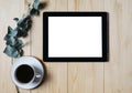 Tablet with a clean blank screen mockup monitor with a branch of eucalyptus and a cup of coffee on a wooden background