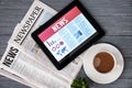 Tablet computer with news on screen and newspapers on wooden background Royalty Free Stock Photo