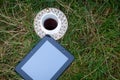 tablet and a cup of coffee on a saucer with gold patterns, stand on the grass, in a clearing Royalty Free Stock Photo