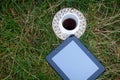 A tablet and a cup of coffee on a saucer with gold patterns, stand on the grass, in a clearing Royalty Free Stock Photo