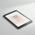 A tablet device lying flat on a white surface displays an e-book cover titled \