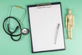Tablet, figurine of a wooden man and stethoscope on light green background, top view and space for text